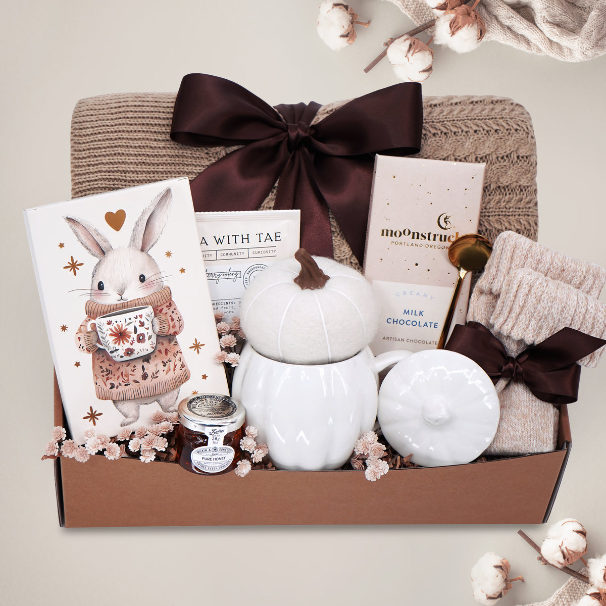Gift basket with a blanket, drink sampler, and decorative items on a light gray background