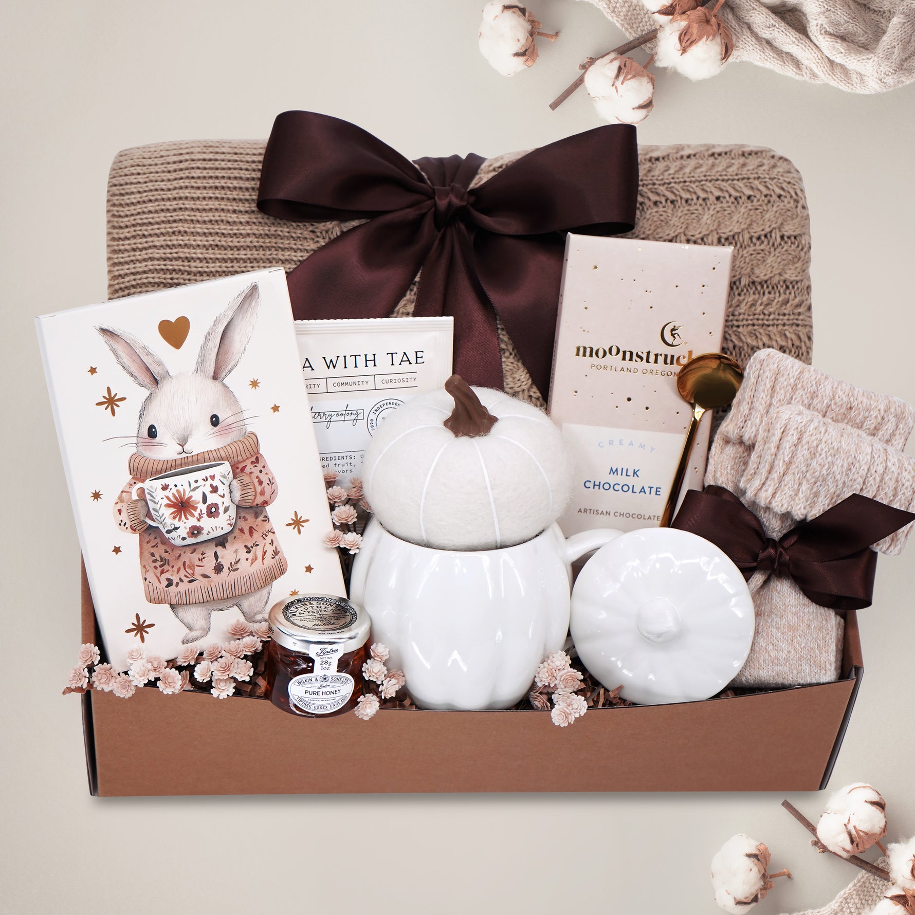Gift basket with a blanket, drink sampler, and decorative items on a light gray background