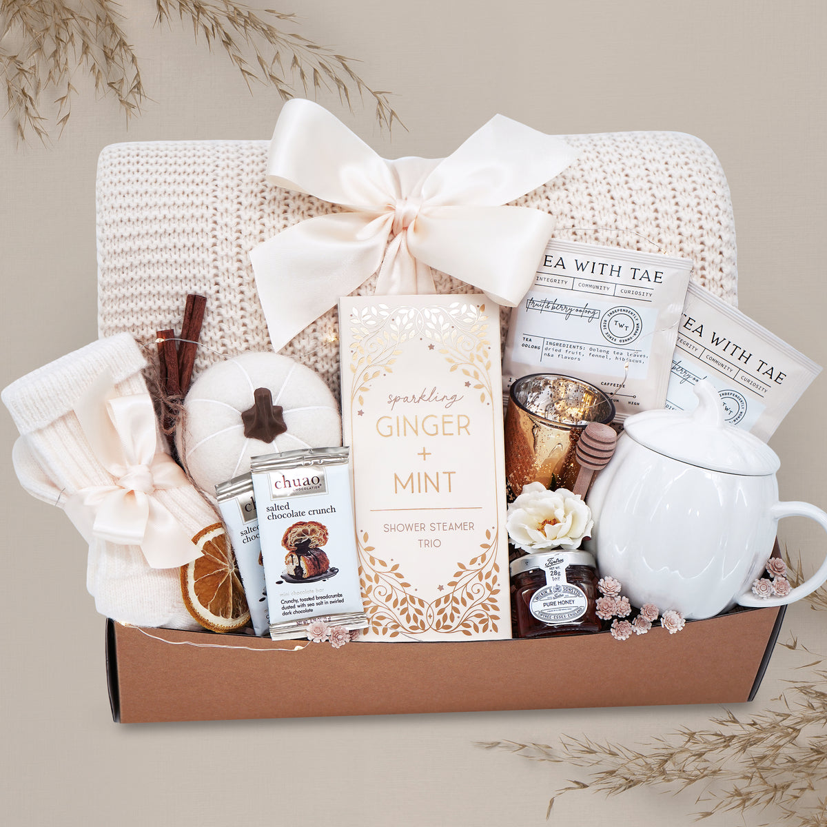 Golden Autumn blanket gift basket with tea, candles, and other items on a gray background