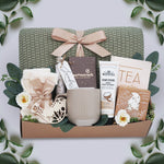 In the Garden Blanket Gift box by Wildflower Pop comes with sage green lace knit blanket, cream knit socks, chocolate bar, floral bath salt tube, grey ribbed mug, hand cream, herbal bath coin, and tea sampler 
