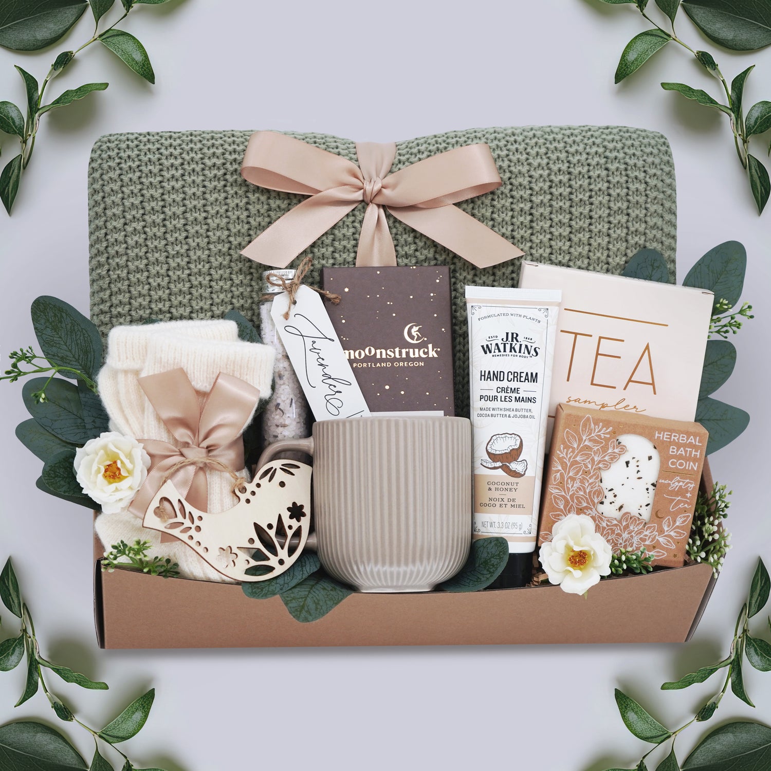 In the Garden Blanket Gift box by Wildflower Pop comes with sage green lace knit blanket, cream knit socks, chocolate bar, floral bath salt tube, grey ribbed mug, hand cream, herbal bath coin, and tea sampler 