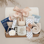 Gift basket with baby items including a mug, rattle, and tea set on a neutral background.