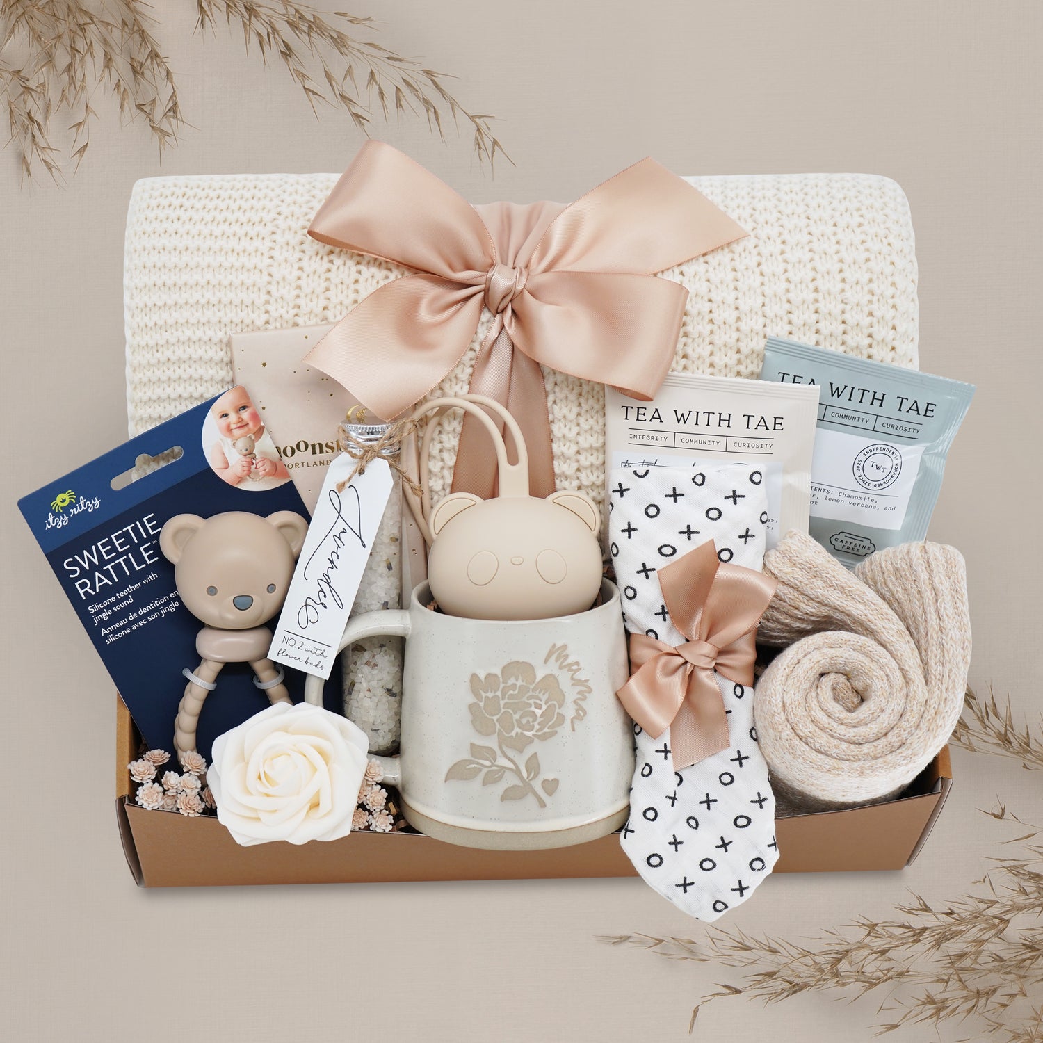 Gift basket with baby items including a mug, rattle, and tea set on a neutral background.