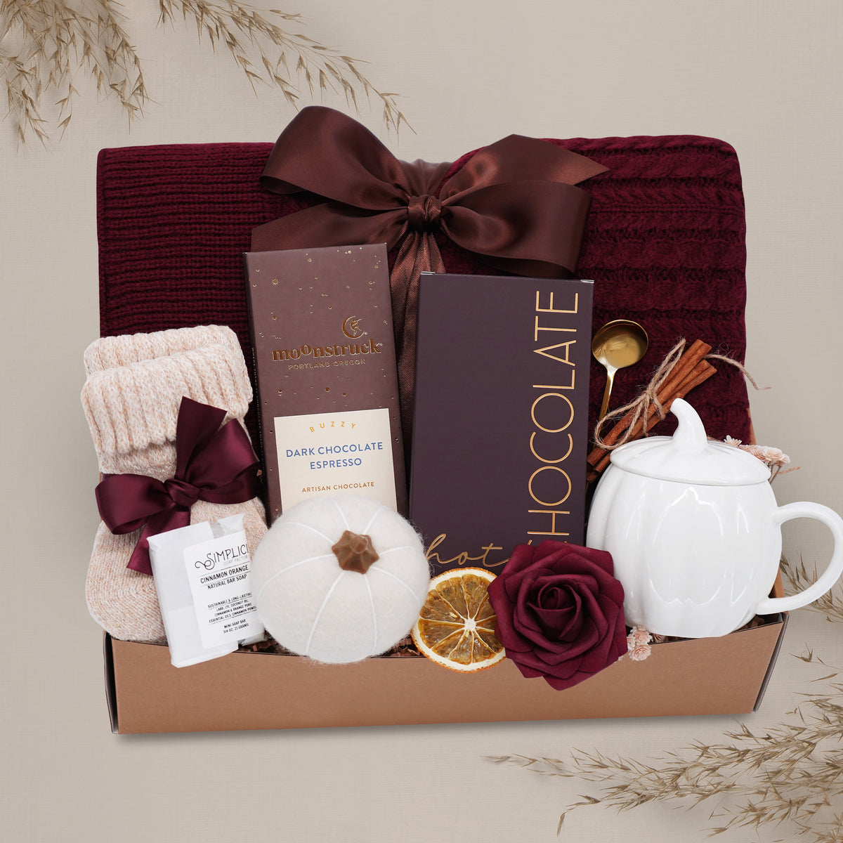 Rustic Retreat blanket gift basket with chocolate, tea set, and other items on a light gray background