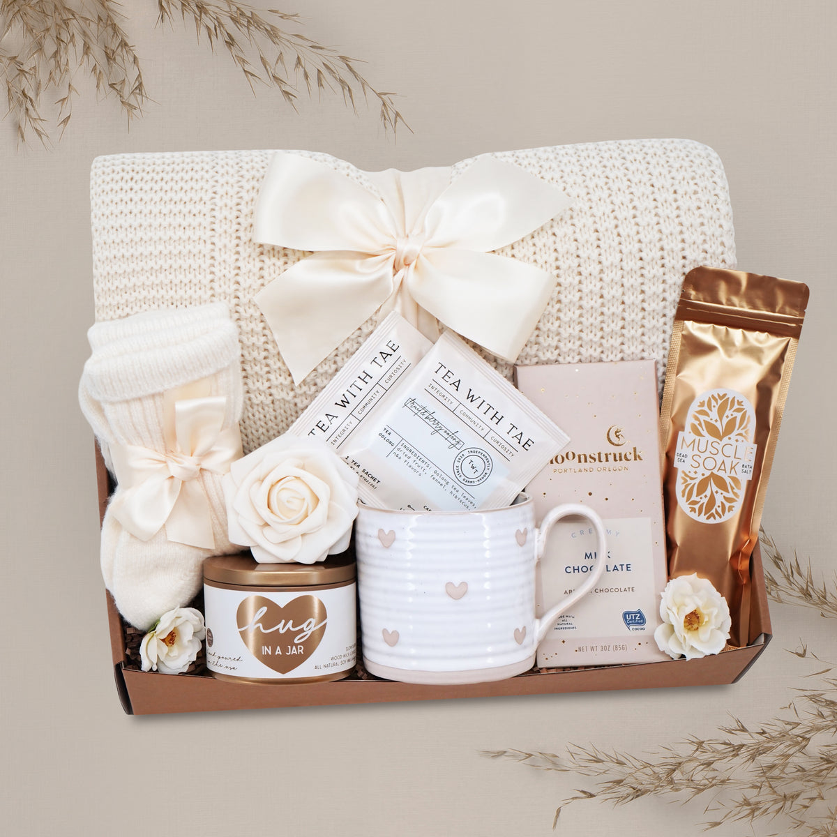 Wildflower Pop Sending a Hug Blanket gift box, with cream lace knit blanket, tea sampler, cream knit socks, hug in a jar soy wax candle, Wildflower Pop Heart ceramic mug, Moonstruck Milk Chocolate bar, and muscle soak