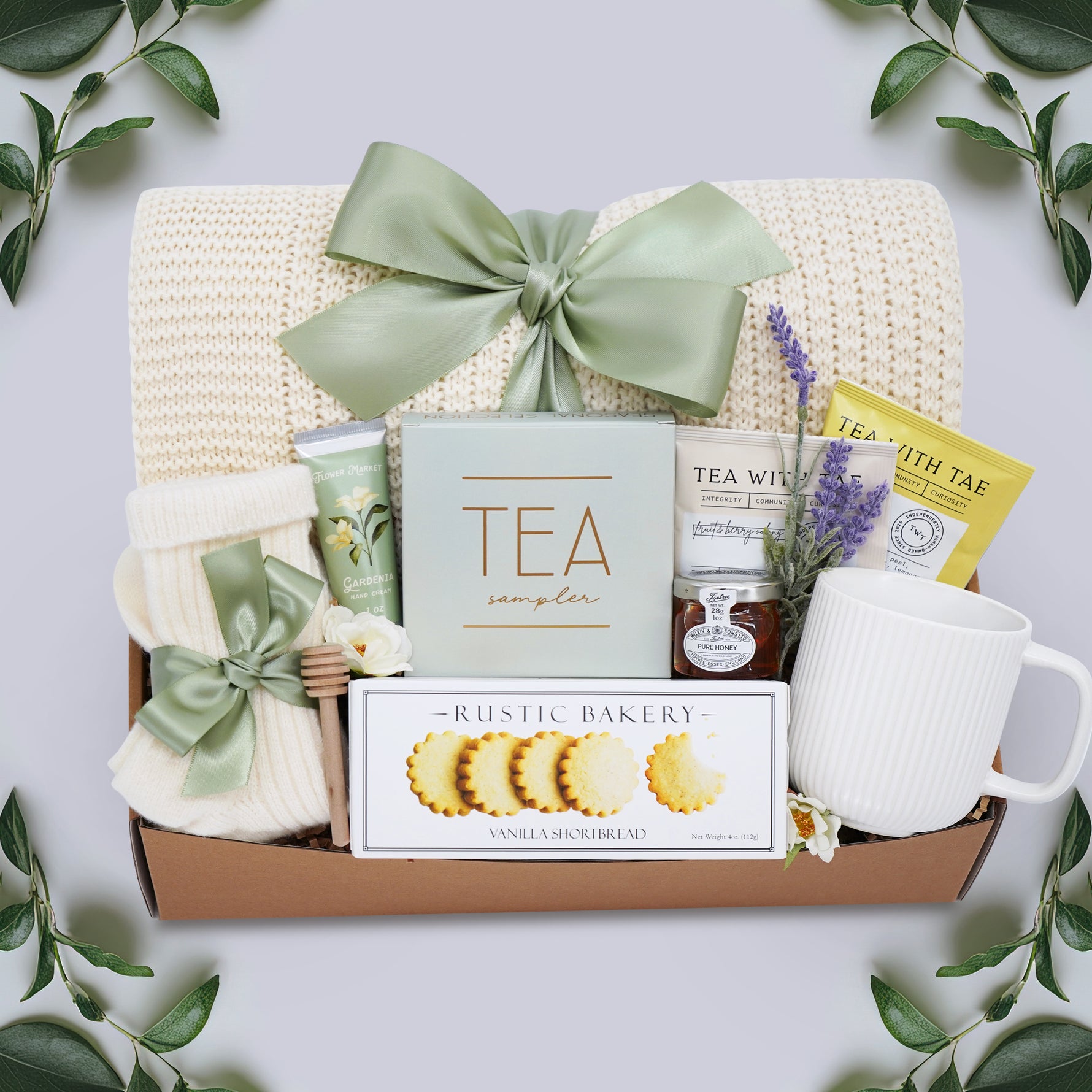 Wildflower Pop Tea Party for One comes with a cream lace knit blanket, cream knit socks, Flower Market Gardenia hand cream, Tea Sampler, Rustic Bakery shortbread cookies, ribbed white ceramic mug, mini honey and dipper