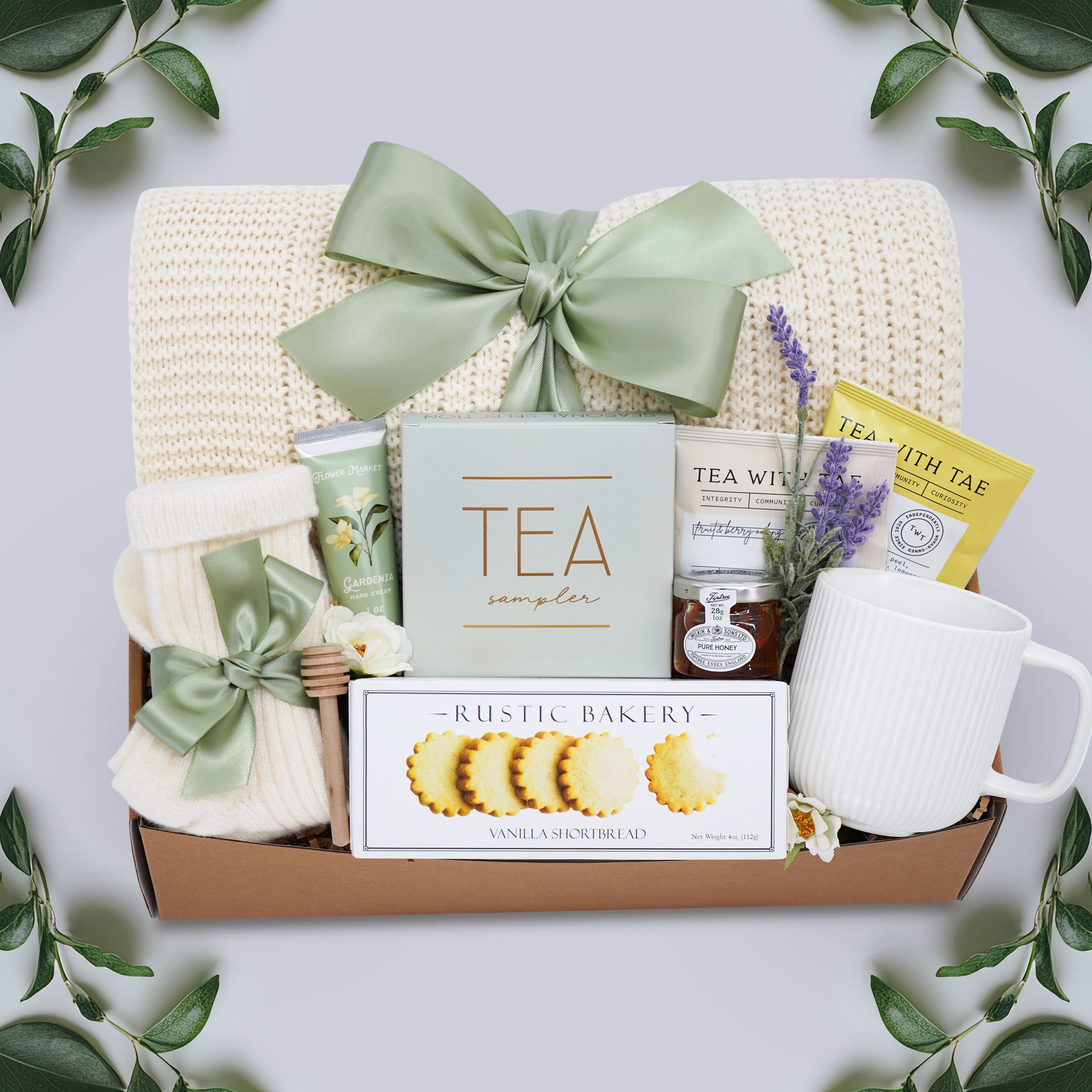 Wildflower Pop Tea Party for One comes with a cream lace knit blanket, cream knit socks, Flower Market Gardenia hand cream, Tea Sampler, Rustic Bakery shortbread cookies, ribbed white ceramic mug, mini honey and dipper