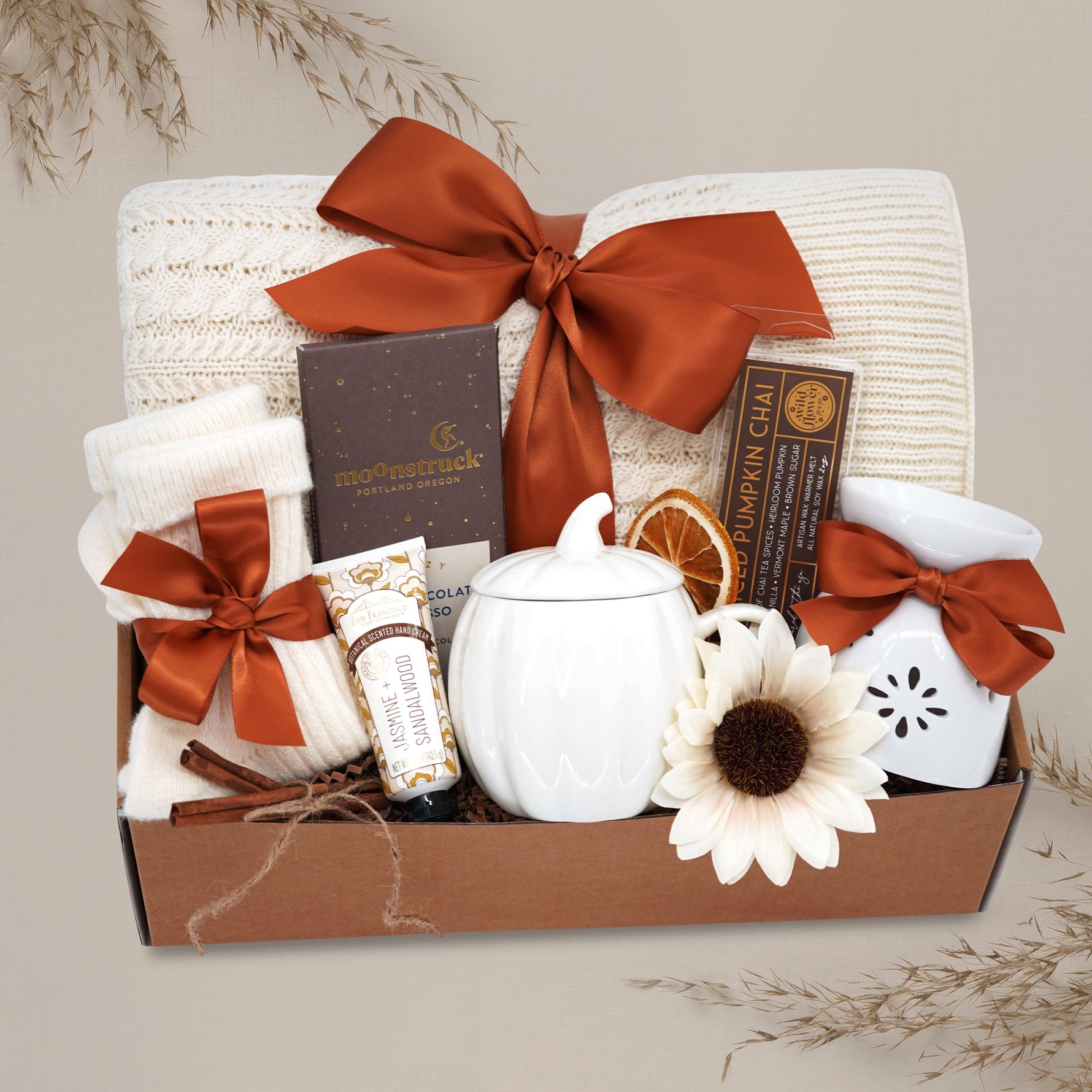 Wildflower Pop Autumn Spice Blanket Gift Box, cream cable knit blanket with pumpkin orange ribbon, chocolate, cream socks, cream pumpkin mug with lid, hand cream, wax warmer and wax melt.