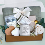 Moms spa retreat blanket box comes with a sage lace knit blanket tied with a cream ribbon, seaside soak bath salts, heart coaster, heart trinket tray. mama ceramic mug, 2 tea with tae tea bags, full size moonstruck milk chocolate bar, cream knit socks, gold demitasse spoon, and faux eucalyptus sprig 