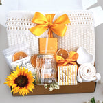 My sunshine blanket box comes with a cream lace knit blanket tied with a yellow ribbon, seaside soak bath salts with orange slices, wavy glass tumbler and straw, full size moonstruck milk chocolate and toffee bar, little drop of sunshine bath bomb, heart trinket tray, and cream knit socks