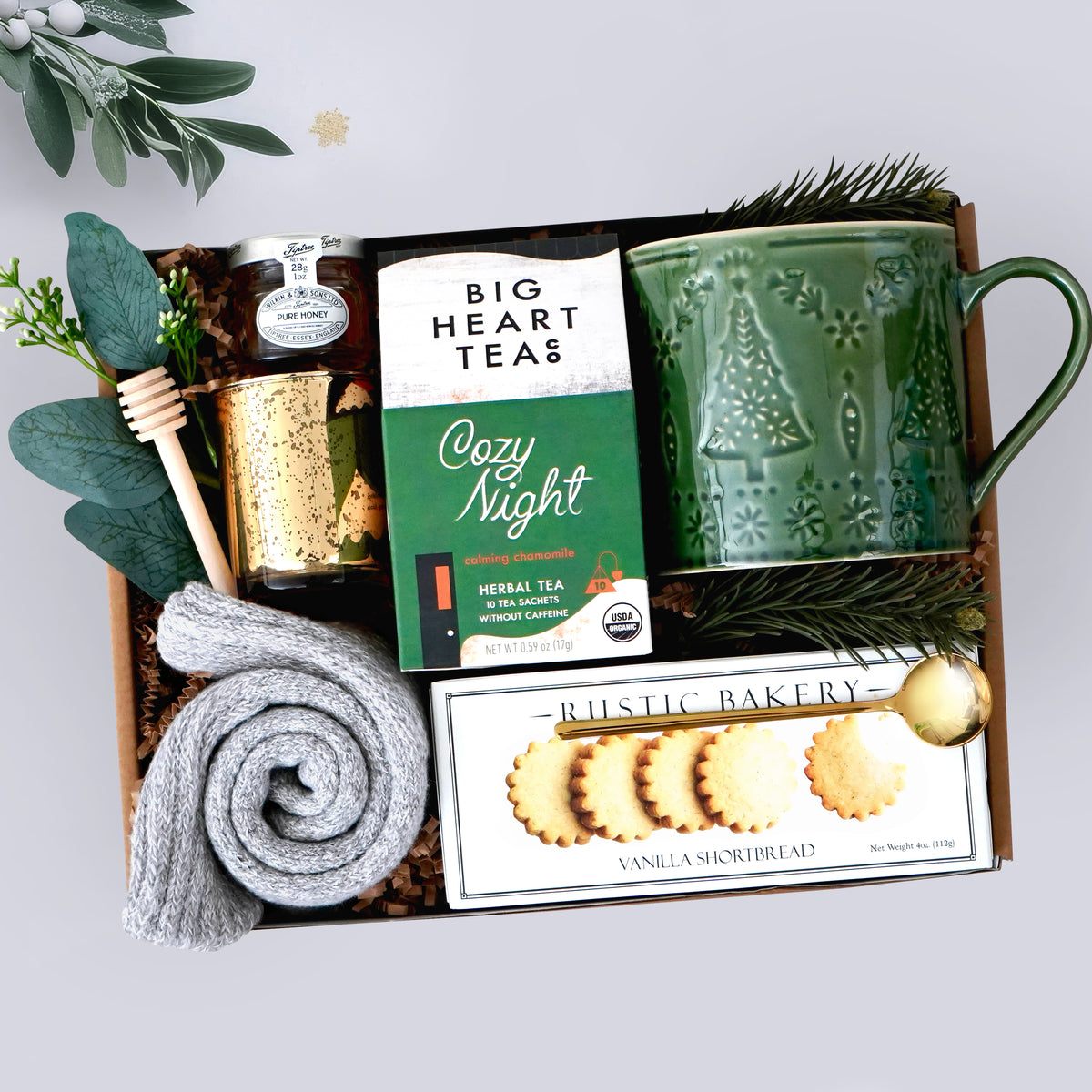 Wildflower Pop Gift set with a green mug, tea packaging, and cookies in a decorative box, grey cozy socks, gold votive, and mini honey and dipper on grey background