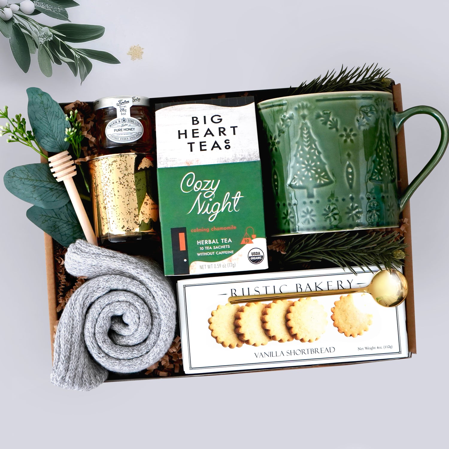 Wildflower Pop Gift set with a green mug, tea packaging, and cookies in a decorative box, grey cozy socks, gold votive, and mini honey and dipper on grey background