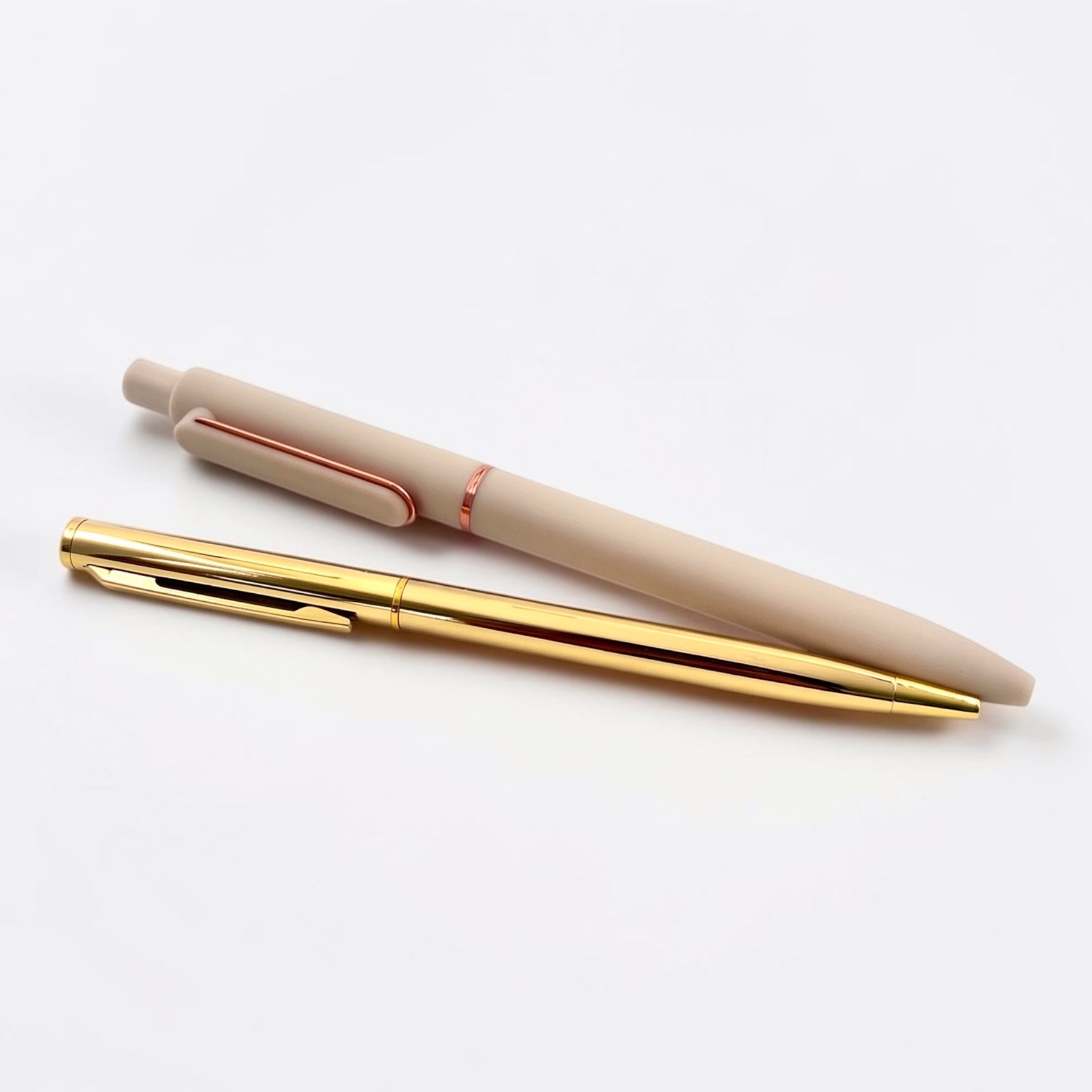 A beige retractable pen and a gold ballpoint pen on a clean white background.