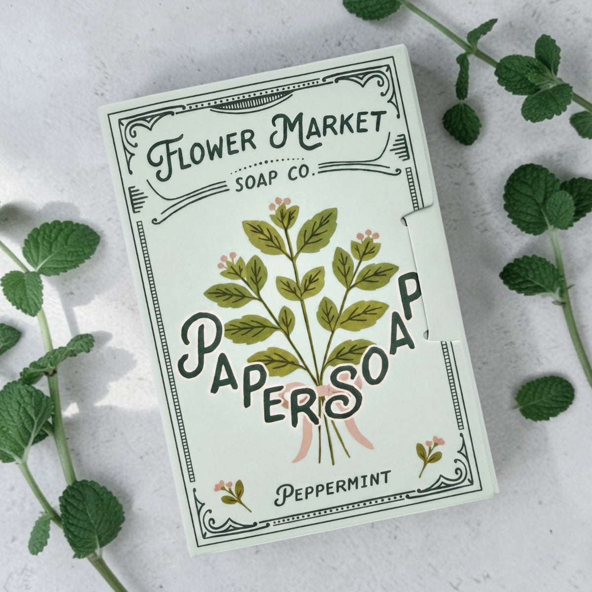 Flower Market Soap Co. Paper Soap sheets. Botanical artwork, Peppermint scent. Photographed on a light stone surface with mint leaves around.