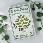 Flower Market Soap Co. Paper Soap sheets. Botanical artwork, Peppermint scent. Photographed on a light stone surface with mint leaves around.