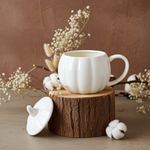 White ceramic pumpkin mug on a wooden block with decorative elements on a brown background