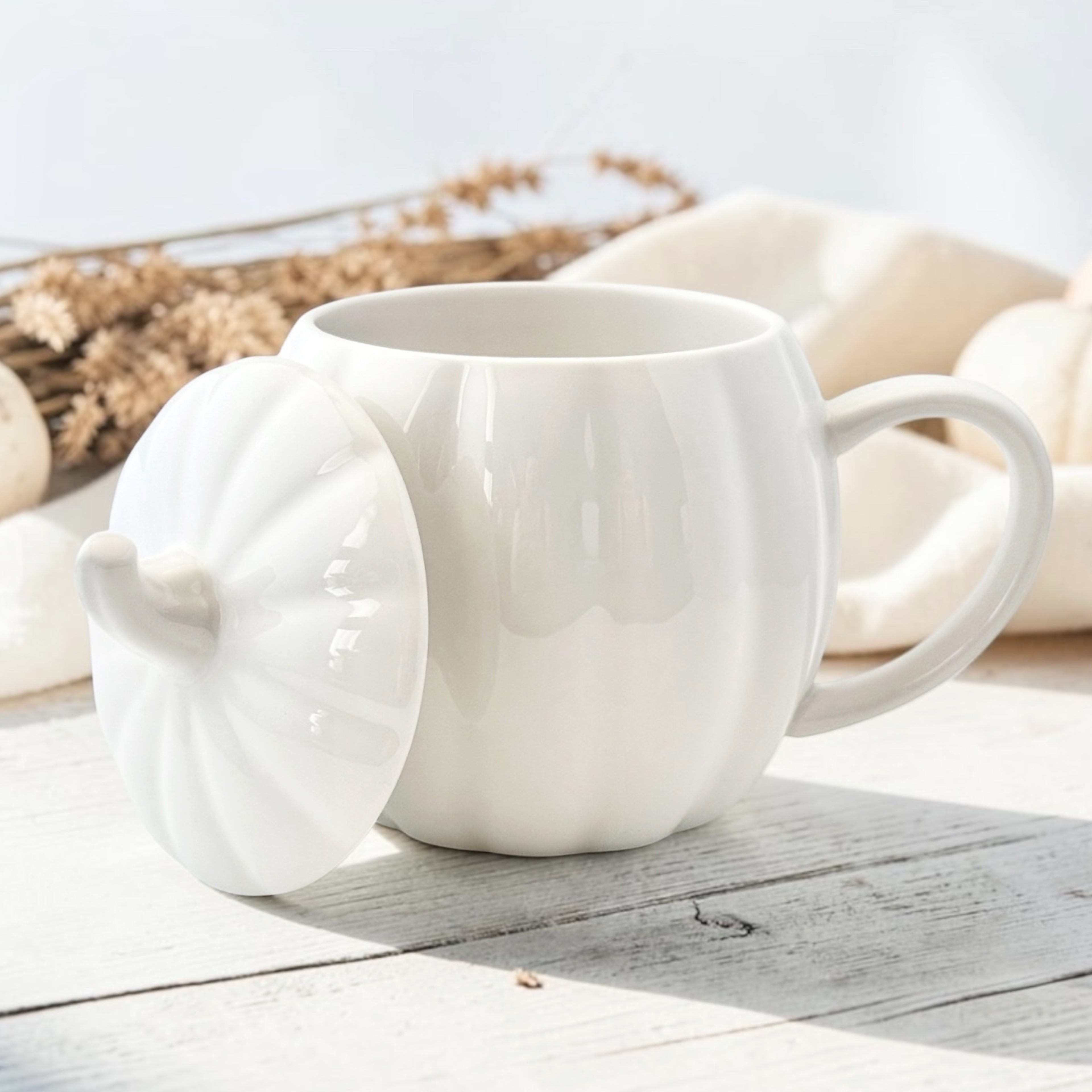 White ceramic pumpkin shaped mug with a matching stem lid on a wooden surface