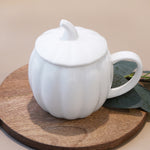 White ceramic pumpkin mug with a lid on a wooden surface