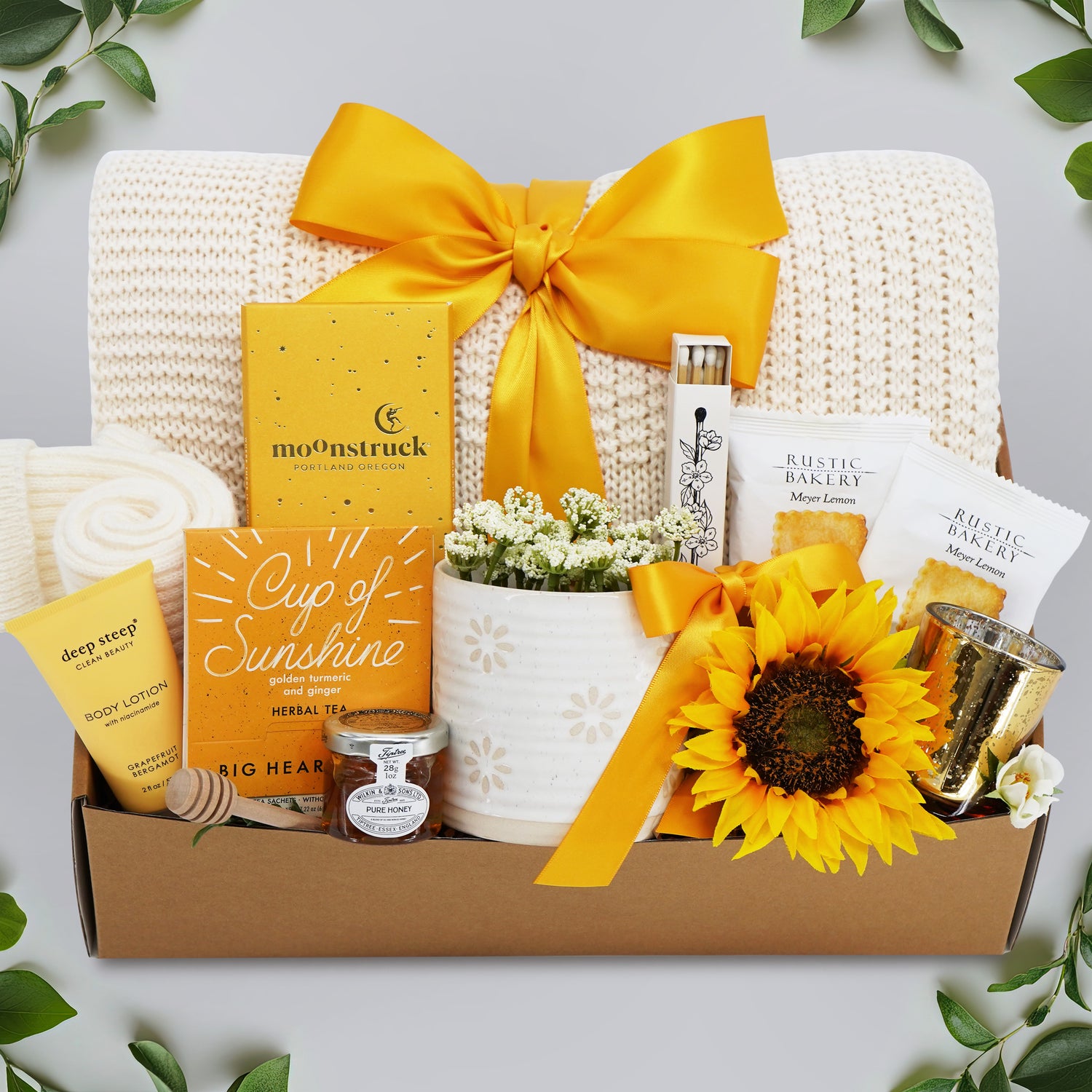 Wildflower Pop Ray of Sunshine Gift Box comes with cream lace knit blanket, moonstruck milk chocolate and toffee bar, Big Heart Tea Cup of Sunshine, Deep Steep grapefruit and bergamot lotion, mini honey and dipper, Wildflower Pop Daisy ceramic mug, faux sunflower, matches, votive and tea light, and 2 rustic bakery short bread cookies 