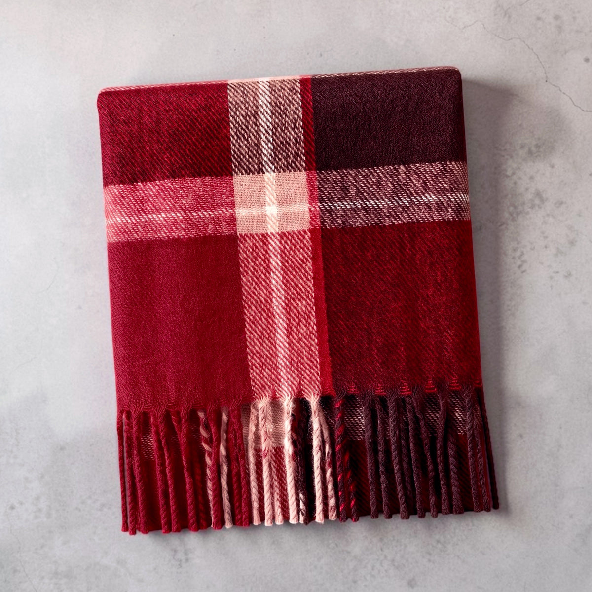 A cozy red plaid scarf with fringe, folded on a light gray textured surface.