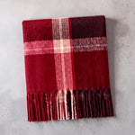 A cozy red plaid scarf with fringe, folded on a light gray textured surface.