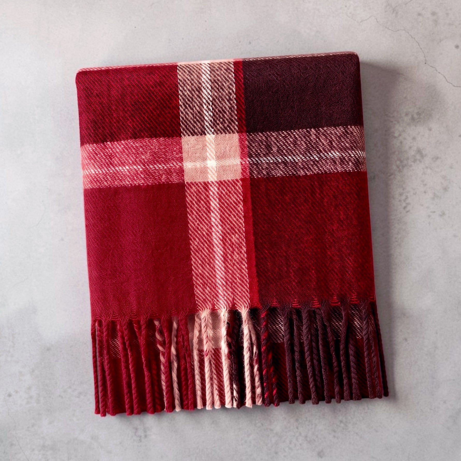 A cozy red plaid scarf with fringe, folded on a light gray textured surface.