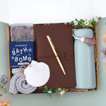 The seaside memories tumbler box comes with a sea foam green insulated tumbler, brown leatherette travelers notebook, gold ball point pen, mariners moon bath bomb, glass votive and tea light, cozy boot socks, and seashell ornament 