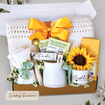Sending Sunshine Gift Box comes with cream lace knit throw tied with sunshine yellow ribbon, tea sampler, tube of bath salts, trail size soy wax candle and matches, toffee and milk chocolate moonstruck bar, cream knit socks, and faux sunflower head. 
