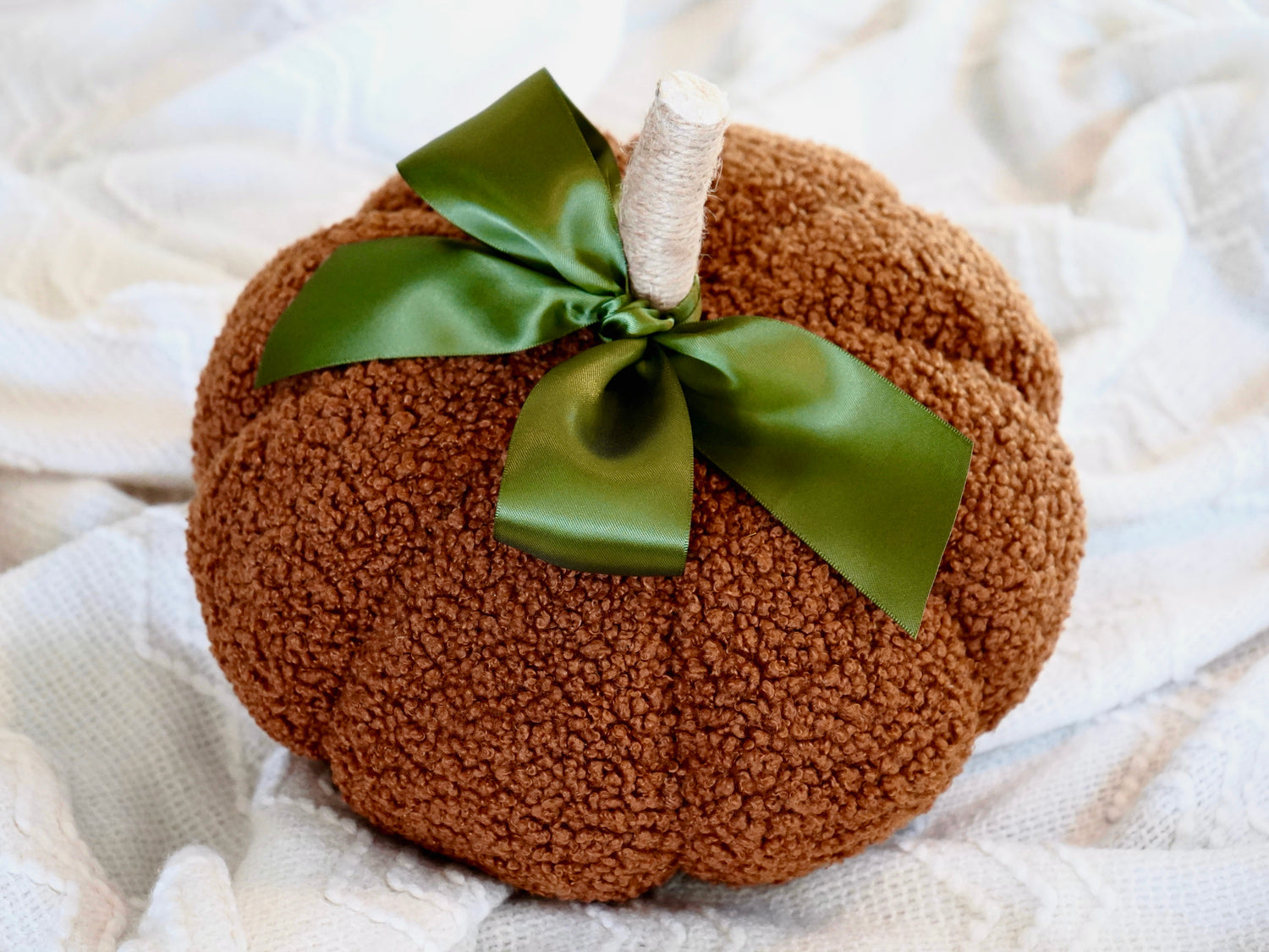 Sherpa Pumpkin Pillow in Orange tied with a moss green bow, measures around 10"