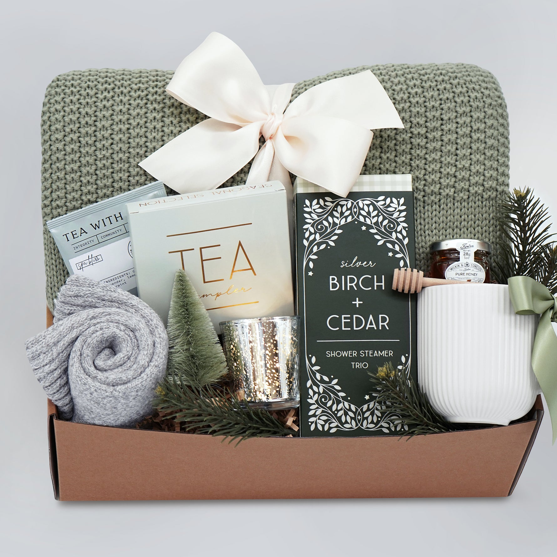 Wildflower Pop Silver Forest Blanket gift box, with sage green lace knit blanket, cream ribbed ceramic mug, grey cozy boot socks, silver votive and tea light, mini honey and dipper, silver birch and cedar shower steamers, and tea sampler