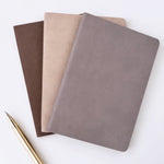 Three faux leather notebooks in brown, beige, and taupe, arranged with a gold pen (not included) on a clean white background.
