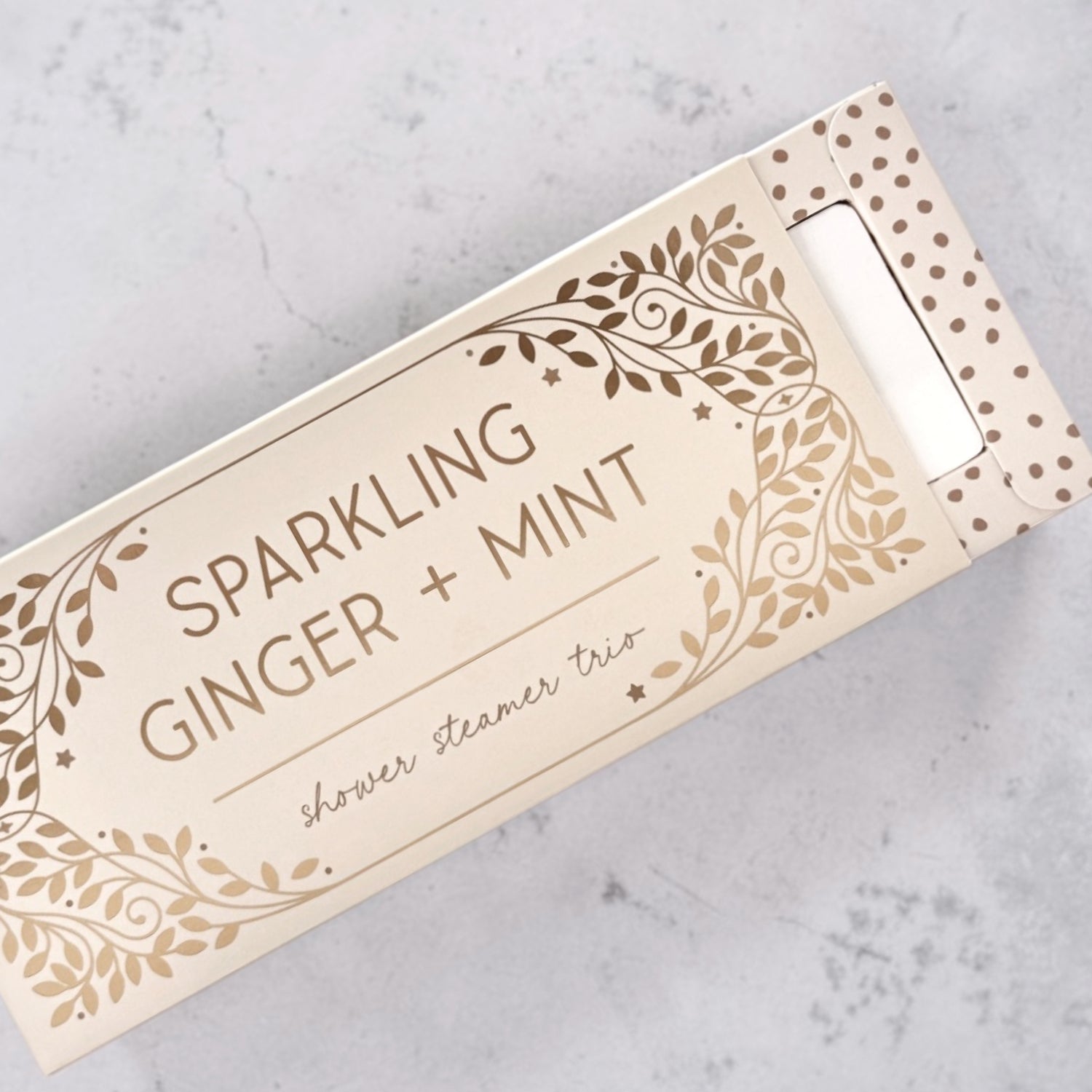 Box of Sparkling Ginger + Mint shower steamers on a gray surface.