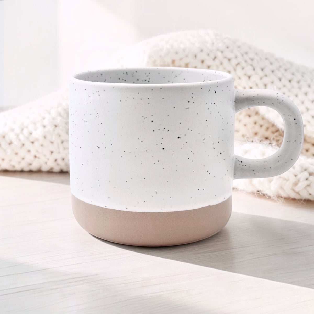 Speckled ceramic mug on a light wooden surface with a blurred textured background