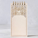 A cream-colored spiral-bound notepad with a decorative floral border in gold and silver foiling. The word 'Notes' are on the cover, shown on a gray background.