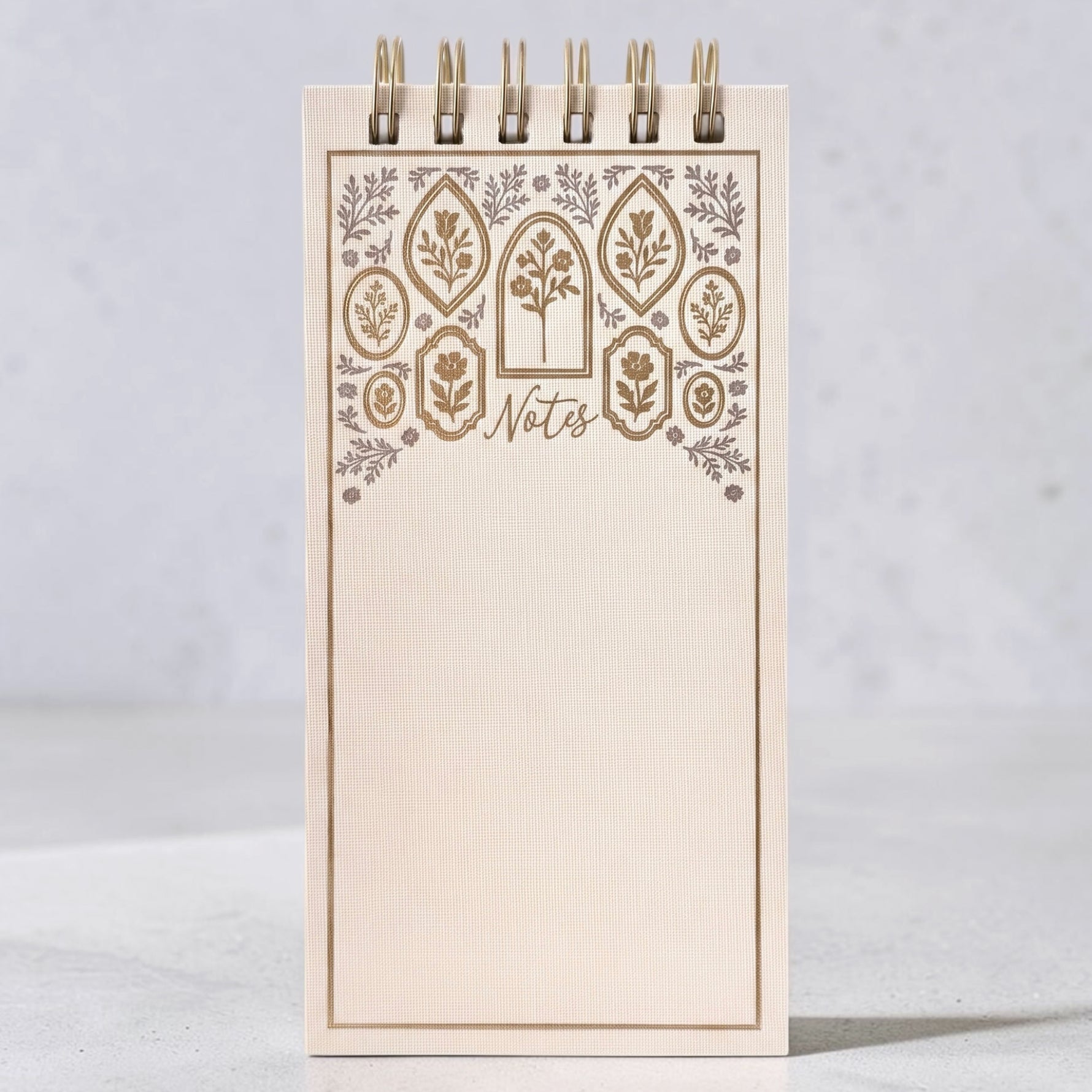 A cream-colored spiral-bound notepad with a decorative floral border in gold and silver foiling. The word 'Notes' are on the cover, shown on a gray background.