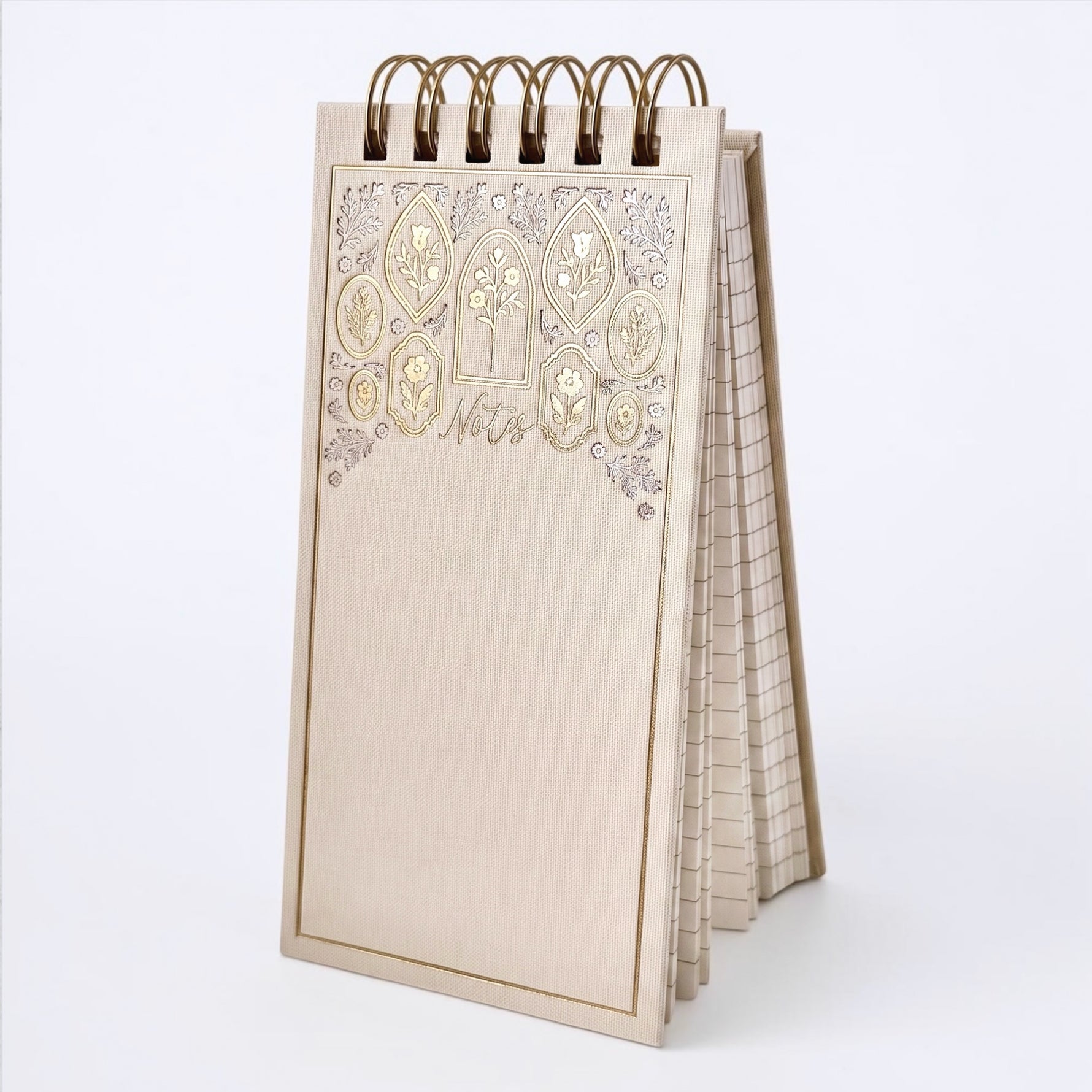 A cream-colored spiral-bound notepad with a decorative floral border in gold and silver foiling. The word 'Notes' are on the cover, shown on a gray background.
