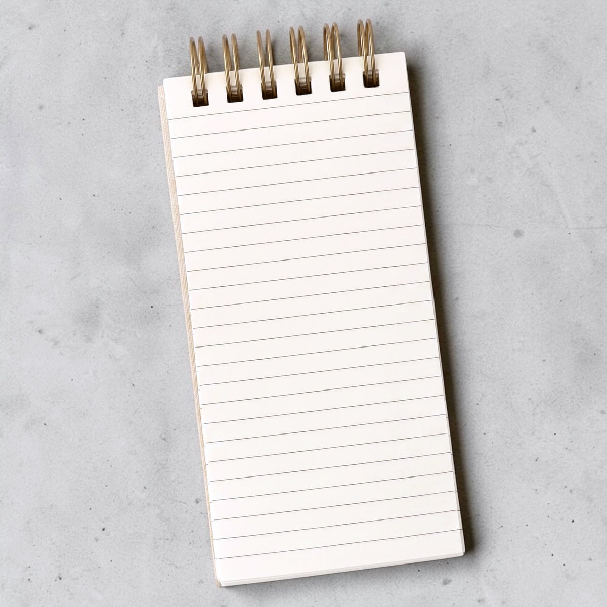 Interior shot of lined notepad with gold-toned wire binding, photographed from above on a light gray textured surface.