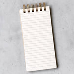 Interior shot of lined notepad with gold-toned wire binding, photographed from above on a light gray textured surface.