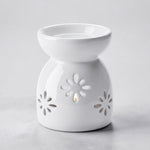 A white ceramic wax warmer/diffuser with a starburst cutout pattern, set against a light gray background.