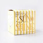 Bath bomb with yellow and white striped box with 'Little Drop of Sunshine' text on a light gray background