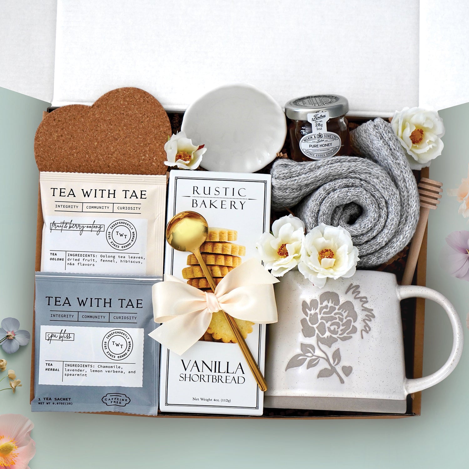 Tea for Mama gift box comes with a Wildflower Pop designed Mama ceramic mug, cozy boot socks, mini honey and dipper, scallop tray, heart coaster, Rustic Bakery vanilla shortbread Cookes, 2 Tea with Tae tea bags, and a gold demitasse spoon