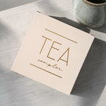 Tea sampler box on a wooden surface with a ceramic mug in the background