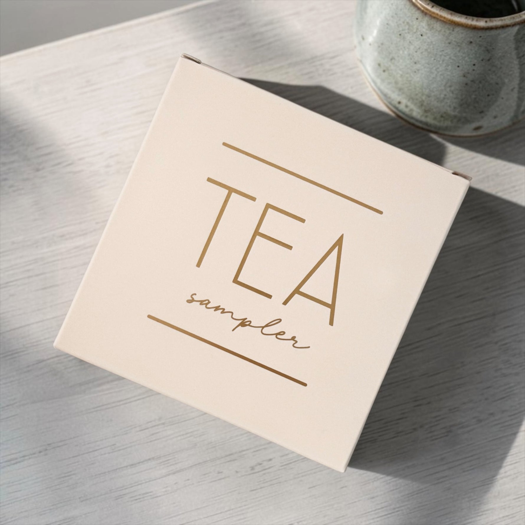 Tea sampler box on a wooden surface with a ceramic mug in the background