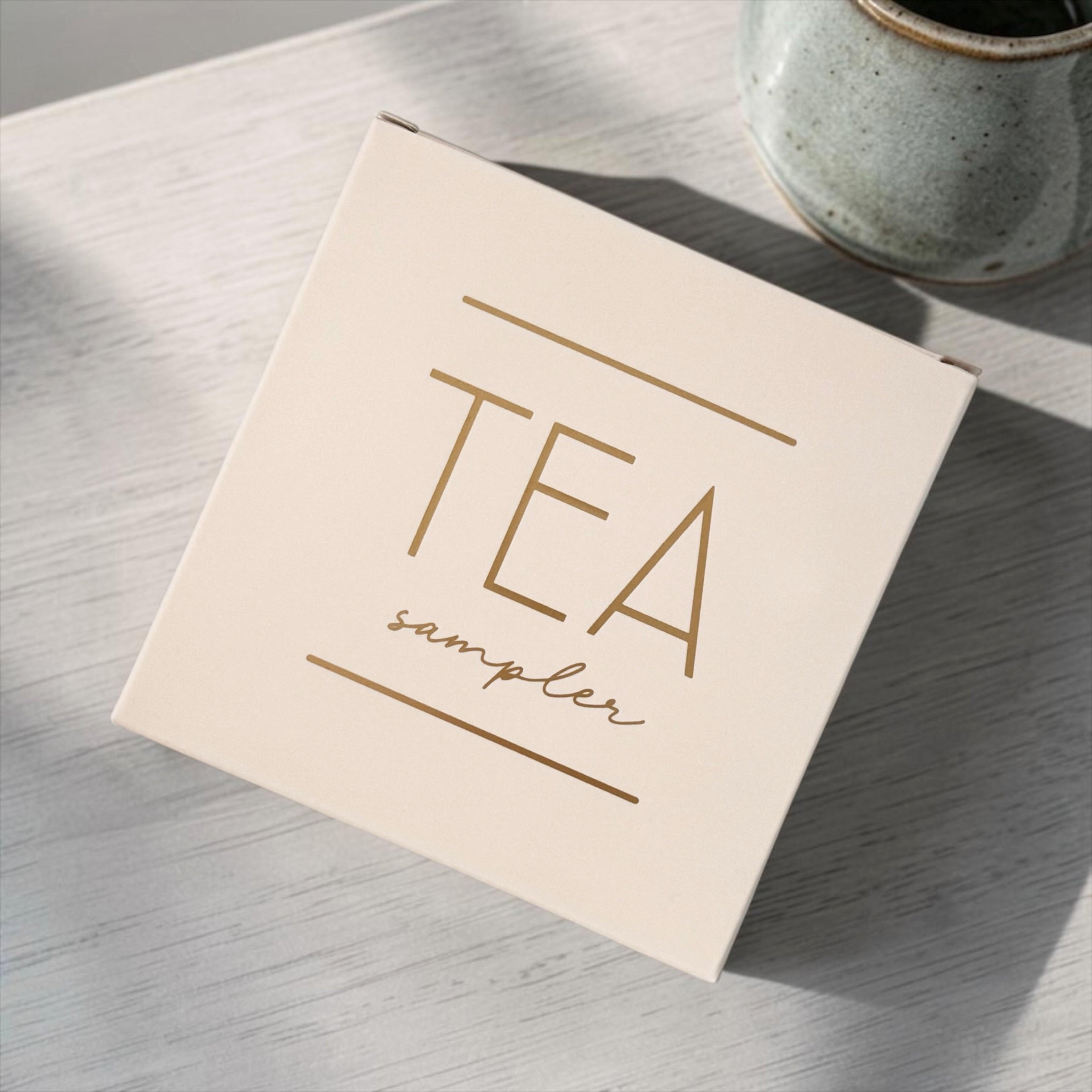 Tea sampler box on a wooden surface with a ceramic mug in the background