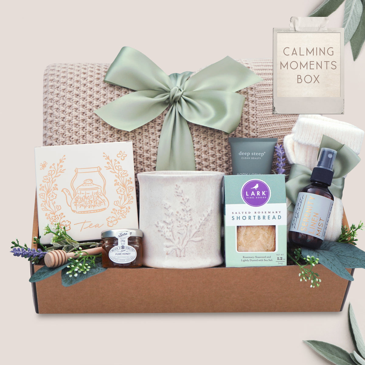 Gift box labeled 'Calming Moments Box' with various items including a honeycomb knit throw, tea, lotion, and cookies.
