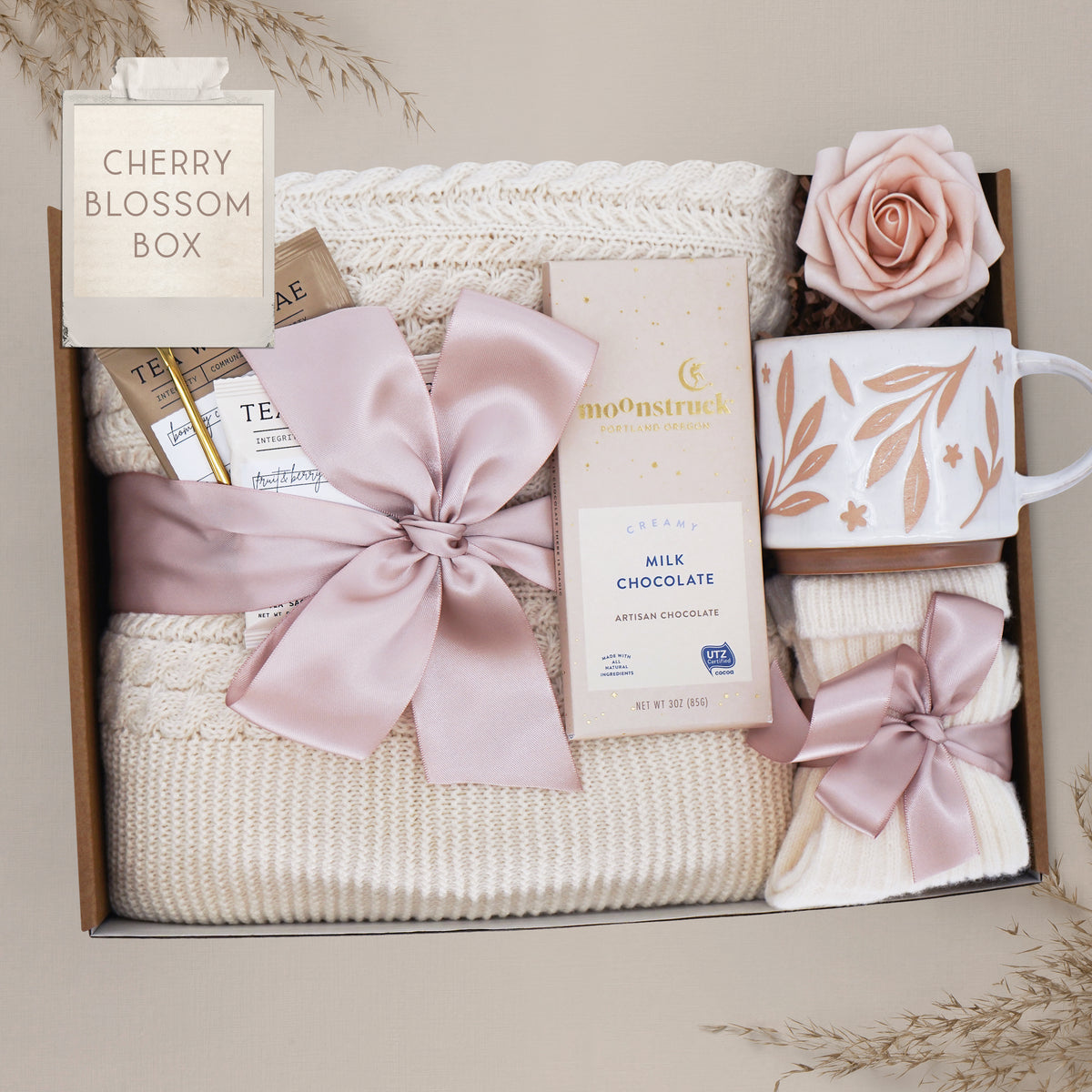 Cream cable knit blanket tied with cherry blossom pink ribbon in gift box