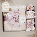 Cream cable knit blanket tied with cherry blossom pink ribbon in gift box