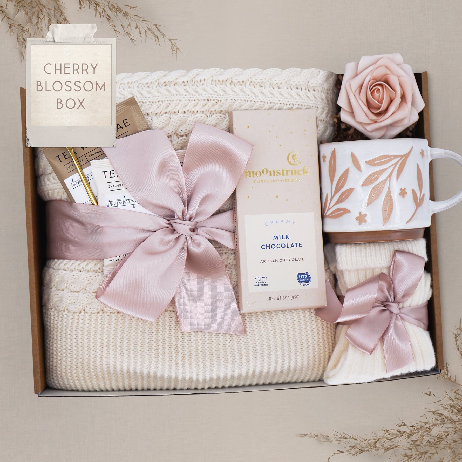 Cream cable knit blanket tied with cherry blossom pink ribbon in gift box