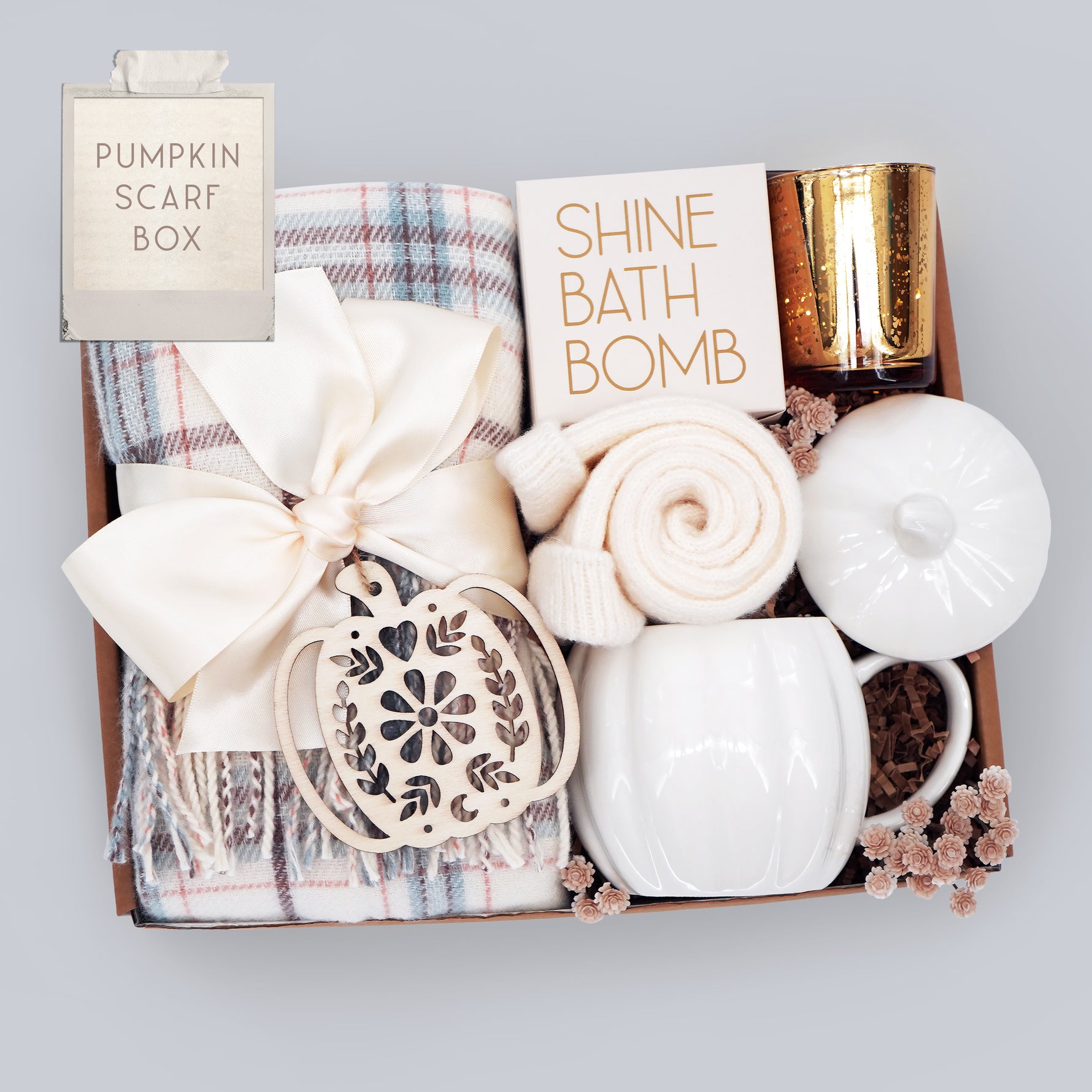 Gift box with a plaid scarf, bath bomb, candle, and other items on a light gray background