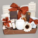 Wildflower Pop Pumpkin Spice Blanket Gift Box, cream cable knit blanket with pumpkin orange ribbon, chocolate, cream socks, cream pumpkin mug with lid, hand lotion, wax warmer and wax melt. On a grey background
